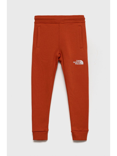 Детски памучен панталон The North Face в оранжево с апликация
